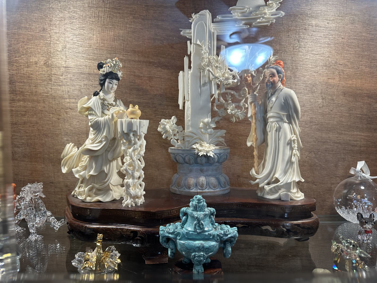 Carved figures on a wooden stand with a turquoise vessel in front.